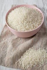 Dry white rice basmati in a pink bowl over white wooden surface, side view. Close-up.