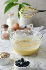 Making pancakes, cake, baking side view of baker hands pouring batter and whisking batter in bowl. Concept of Cooking ingredients and method on white marble background, Dessert recipes and homemade.