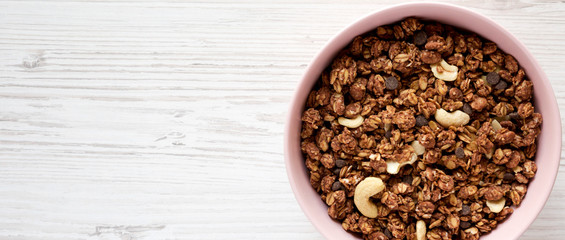 Homemade chocolate granola with nuts in a pink bowl, overhead view. From above, top view, flat lay. Copy space.