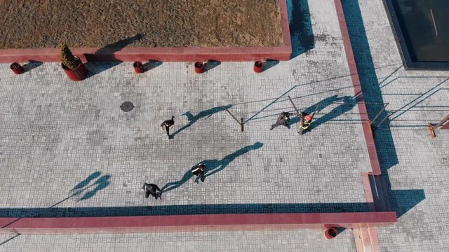Three athletic young men overcoming obstacles and running from the grass on the road performing tricks. Aerial view