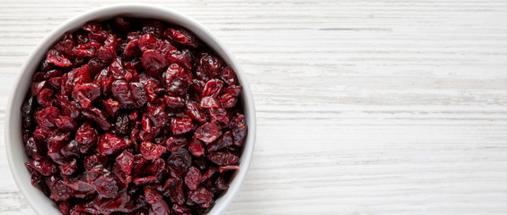 Dry organic cranberries in a gray bowl over white wooden surface, top view. Overhead, from above, flat lay. Copy space.