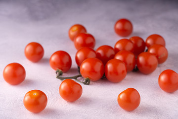 Bunch of cherry tomatoes on white textured stone concrete table, side view with copy space. Ingredients for cooking.