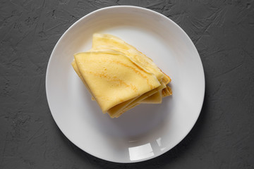 Top view, pile of tasty blini on a white plate over gray background. Flat lay, overhead, from above. Close-up.