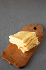 Pile of tasty blini on a rustic wooden board over concrete surface, side view. Copy space.