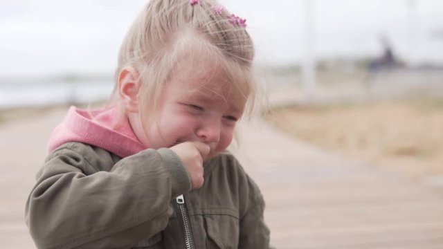 The little girl is crying outside. The child lost his parents and roars on the street. The girl in the jacket is crying in the park by the sea