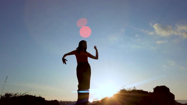Silhouette di una ballerina che danza in cima a una montagna al tramonto con sfondo cielo. Rallentatore