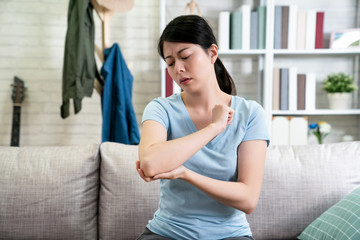 unhappy young asian woman with elbow pain indoors. office syndrome health care concept. upset...