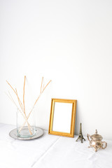 Dried flower in glass vase, empty gold vintage photo frame, eiffel tower miniature on white table top on white wall background in natural light with empty copy space. Minimal interior design concept.