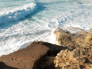 Empty long wide beach, yellow sand; curling crushing waves ; sunny weather in Nazare, Portugal; nature background; windy and wavy beach with surf camp; nature power; dangerous cliff