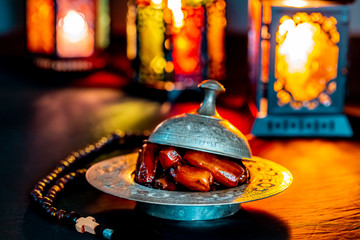 The Muslim feast of the holy month of Ramadan Kareem with dates on a tray on a dark background. Beautiful background with a shining lantern Fanus.