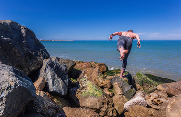 Fototapeta na wymiar Young caucasian man practices yoga on the rocks by the beach