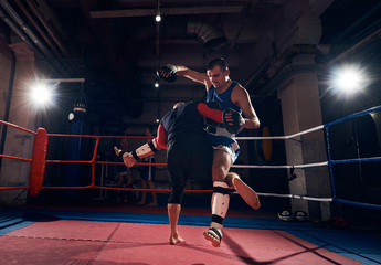 athletic sportsman fighter practicing mma with his trainer, fighting in the ring at the health club