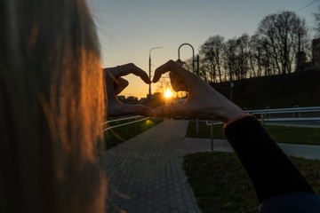 Naklejka na ściany i meble Blond woman holding hands as heart shape with beautiful sky in a warm color sunset