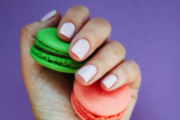 Hand with light rose manicure with colorful macarons. Isolated at bright purple background.