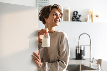 Happy brunette woman drinking milk and looking away - obrazy, fototapety, plakaty