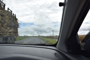 Fototapeta na wymiar Estrada vista de dentro de um carro. Caminhão, estrada, campo verde e céu azul. 