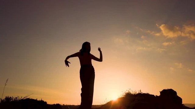 Silhouette di una ballerina che danza in cima a una montagna al tramonto con sfondo cielo. Rallentatore