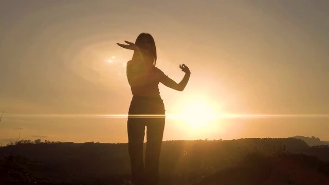 Silhouette di una ballerina che danza in cima a una montagna al tramonto con sfondo cielo. Rallentatore