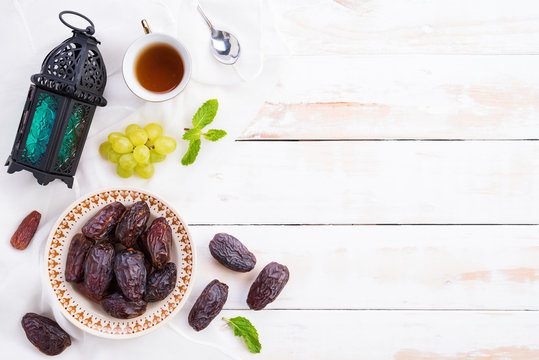 Ramadan Food And Drinks Concept. Ramadan Lantern With Tea, Dates Fruit, Grape And Mint Leaves On A White Wooden Table Background. Top View, Flat Lay.