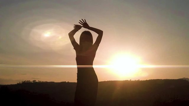 Silhouette di una ballerina che danza in cima a una montagna al tramonto con sfondo cielo. Rallentatore