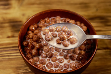 Cereal chocolate balls with milk in a bowl on wooden table. Spoon with breakfast