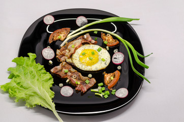 fried eggs on a black dish decorated with green vegetables, tomatoes and spices