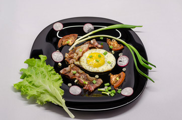 fried eggs on a black dish decorated with green vegetables, tomatoes and spices