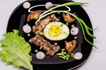 fried eggs on a black dish decorated with green vegetables, tomatoes and spices