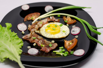 fried eggs on a black dish decorated with green vegetables, tomatoes and spices