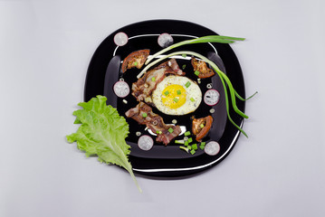 fried eggs on a black dish decorated with green vegetables, tomatoes and spices