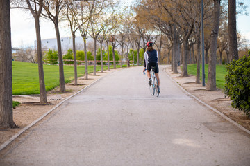 Back view of young male cyclist in sportswear and protective helmet cycling bike on road in park