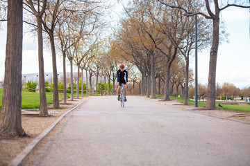 Young handsome male cyclist in sportswear and protective helmet cycling bike on road in park