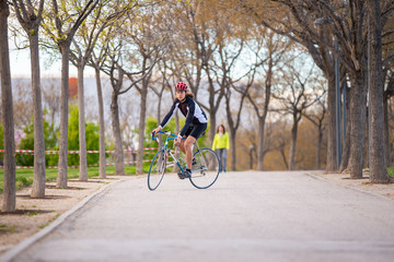 Fototapeta premium Young handsome male cyclist in sportswear and protective helmet cycling bike on road in park