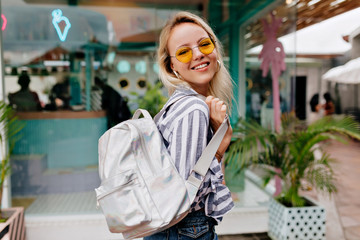 Smiling happy stylish girl in round fashionable spectaculars wearing stripped shirt with white backpack 