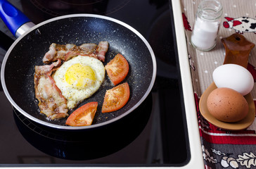 simple home-cooked food, omelet with tomatoes and bacon in a frying pan on a ceramic electric stove