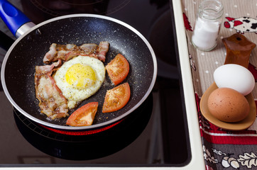 simple home-cooked food, omelet with tomatoes and bacon in a frying pan on a ceramic electric stove