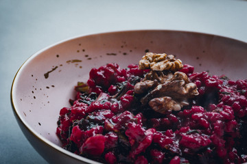 Beetroot and barely risotto with walnuts served in a pink bowl with golden rim on blue/grey...