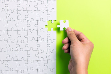 Hand putting the last piece of white jigsaw puzzle on green background and place for your content
