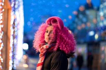 Portrait young attractive caucasian girl model with afro style curly bright pink hair, tattooed face. Evening downtown walking