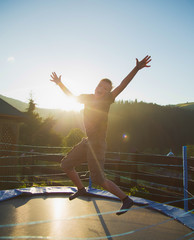 Fototapeta na wymiar Young kid cheerfully jumping on trampoline outdoors at countryside during summer vacations.