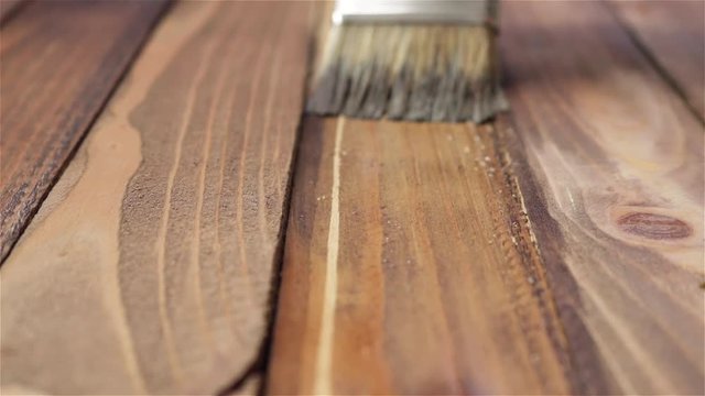 hand in rubber glove with paintbrush painting wooden plank board depth of field