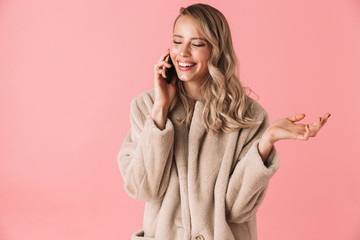 Smiling blonde woman wearing in fur coat talking by smartphone