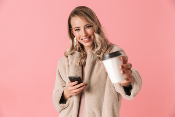 Happy blonde woman wearing in fur coat holding smartphone