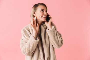 Cheerful blonde woman wearing in fur coat talking by smartphone