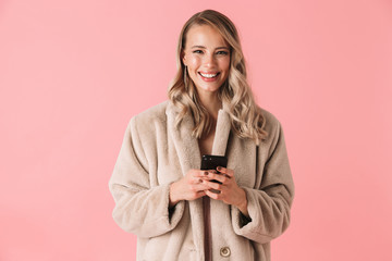Happy blonde woman wearing in fur coat holding smartphone