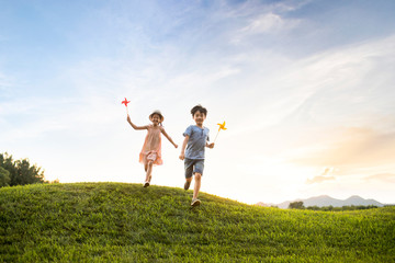 Two children playing paper windmill on meadow