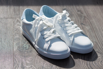 White leather female sneakers shoes on laces on grey brown wooden background.