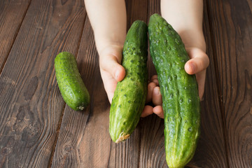 children's hands holding fresh cucumbers on a wooden table, healthy food concept