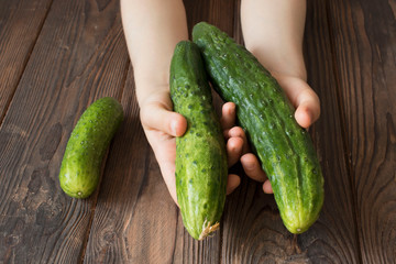 children's hands holding fresh cucumbers on a wooden table, healthy food concept