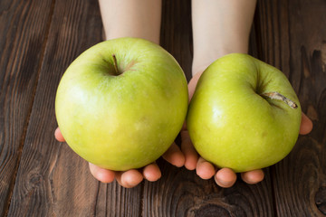 children's hands holding green apples on a wooden table, healthy food